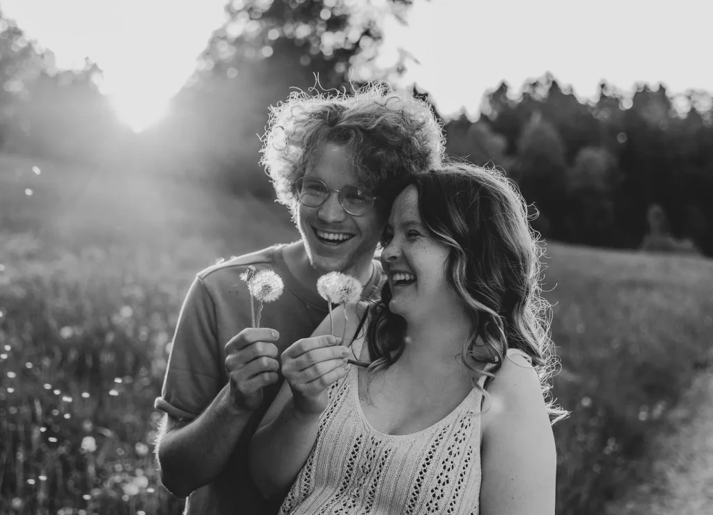 Die Schwarz-Weiss-Aufnahme von Katja Stumbeck aus Straubing zeigt eine schwangere Frau und ihren Partner, wie sie draußen auf einem Feldweg im bayerischen Wald Pusteblumen in der Hand halten