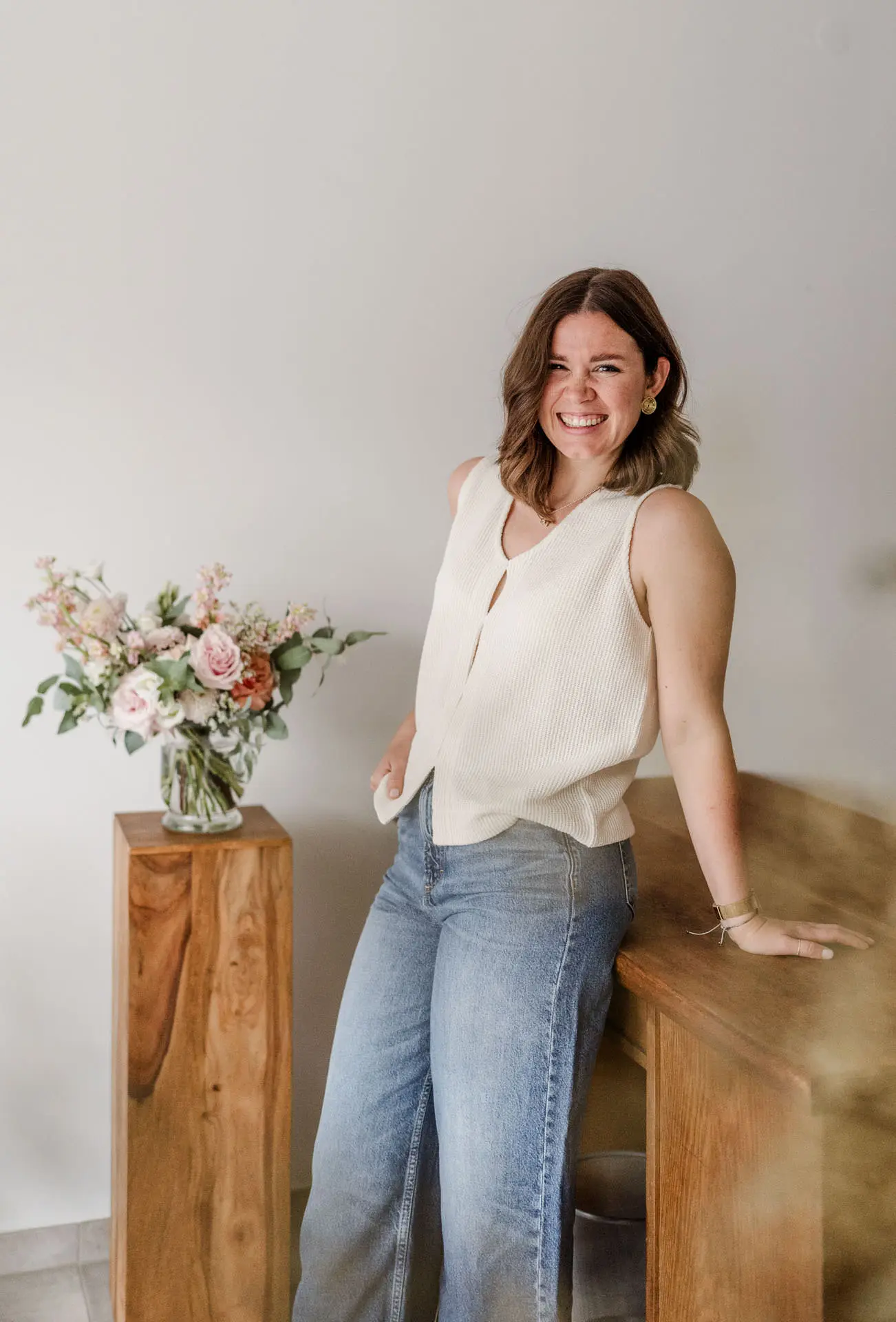 Die Fotografin Katja Stumbeck aus Straubing stütz sich auf einem Regal aus Holz ab und neben ihr steht auf einem Pfahl ein schöner bunter Blumenstrauß