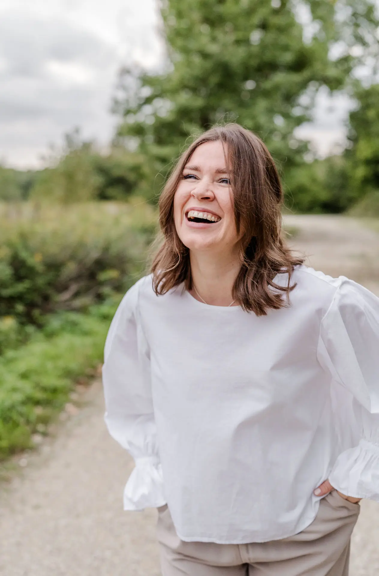 Die Fotografin Katja Stumbeck steht draußen in der Natur auf einem Kiesweg und lacht freundlich in die Kamera