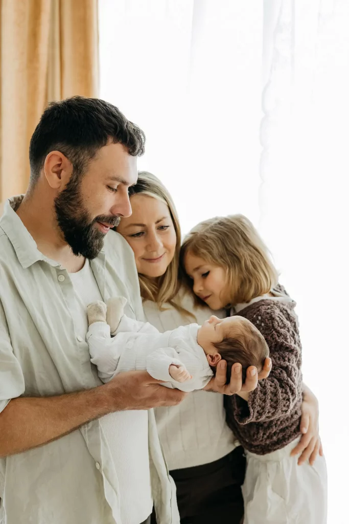 Mann hält Baby in den Händen, Frau daneben hält die ältere Töchter am Arm