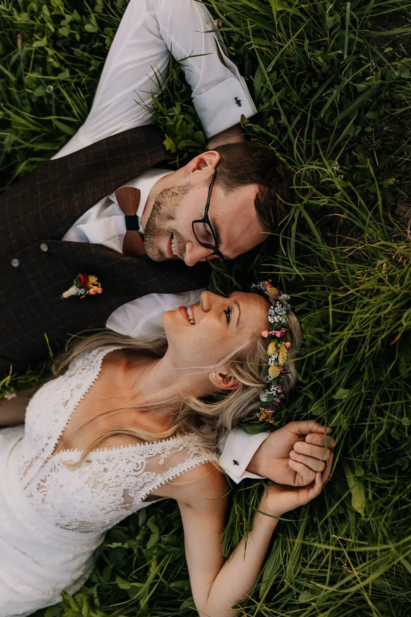 Ein Mann und eine Frau, die gerade im Bayerischen Wald geheiratet haben, liegen im Gras und halten sich an der Hand