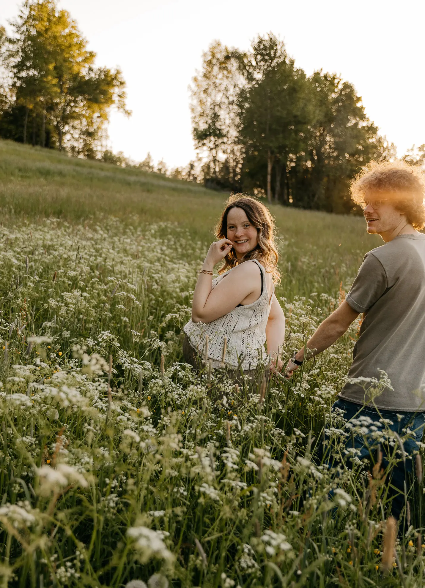 Eine schwangere Frau geht mit ihrem Partner an der Hand durch eine Wiese voller Blumen und wird dabei von Fotografin Katja Stumbeck begleitet
