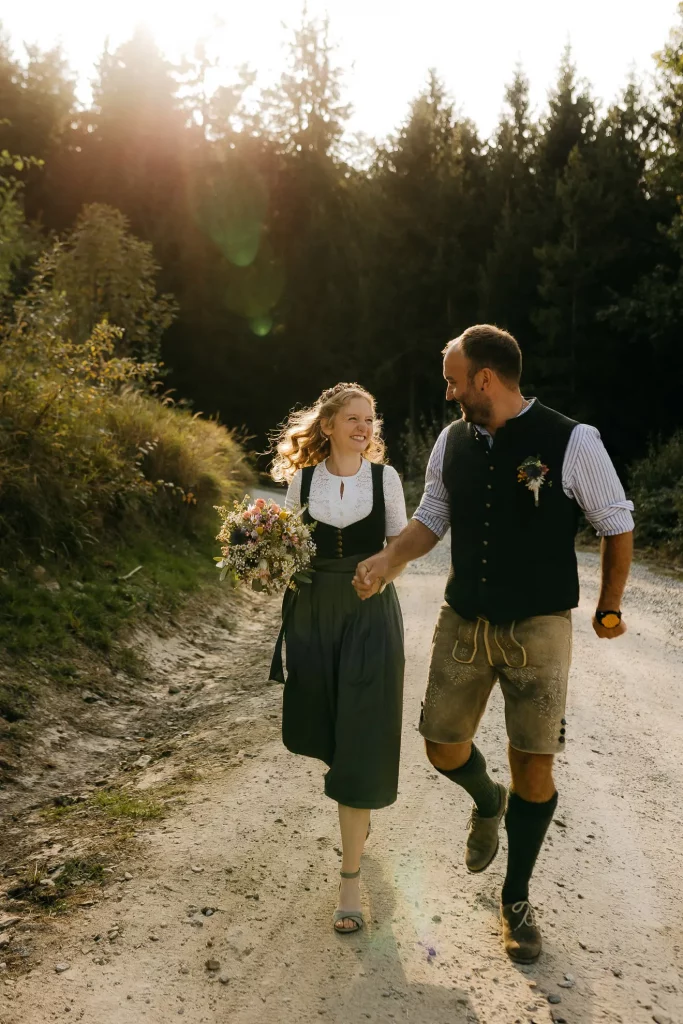 Ein Brautpaar in fescher Tracht schaut sich beim Gehen auf einem Waldweg in die Augen und genießt die schöne Atmosphäre des Bayerischen Waldes