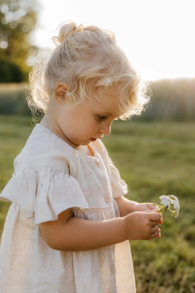 Ein Mädchen im Kleinkindalter blickt auf die gepflückten Blumen in ihrer Hand fotografiert von Familienfotografin Katja Stumbeck
