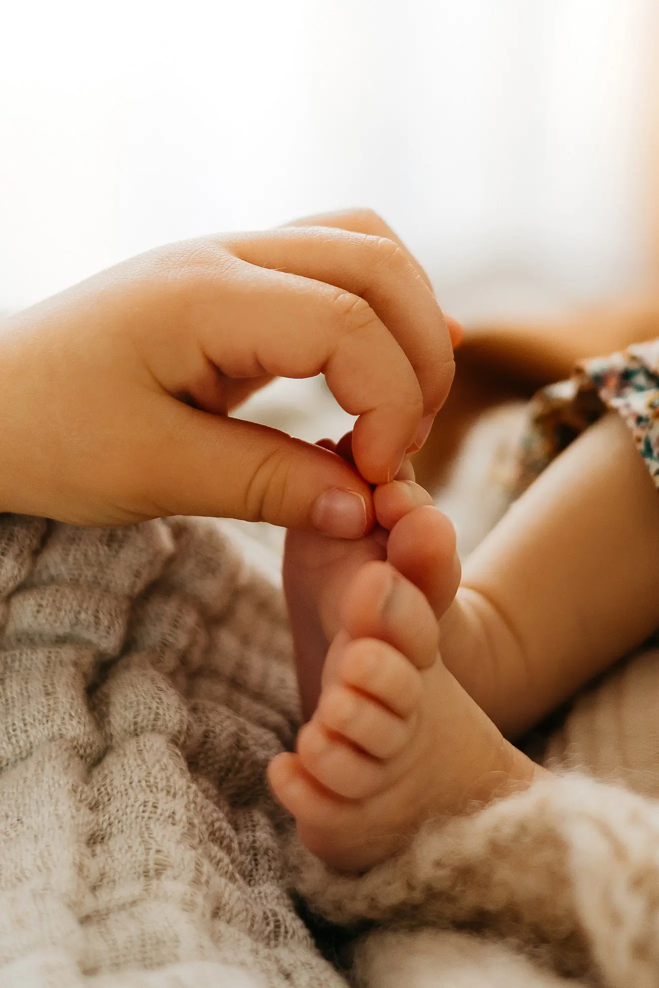 Eine Kinderhand berührt die kleinen nackten Zehen eines neugeborenen Babys in Straubing und streichelt sie vorsichtig