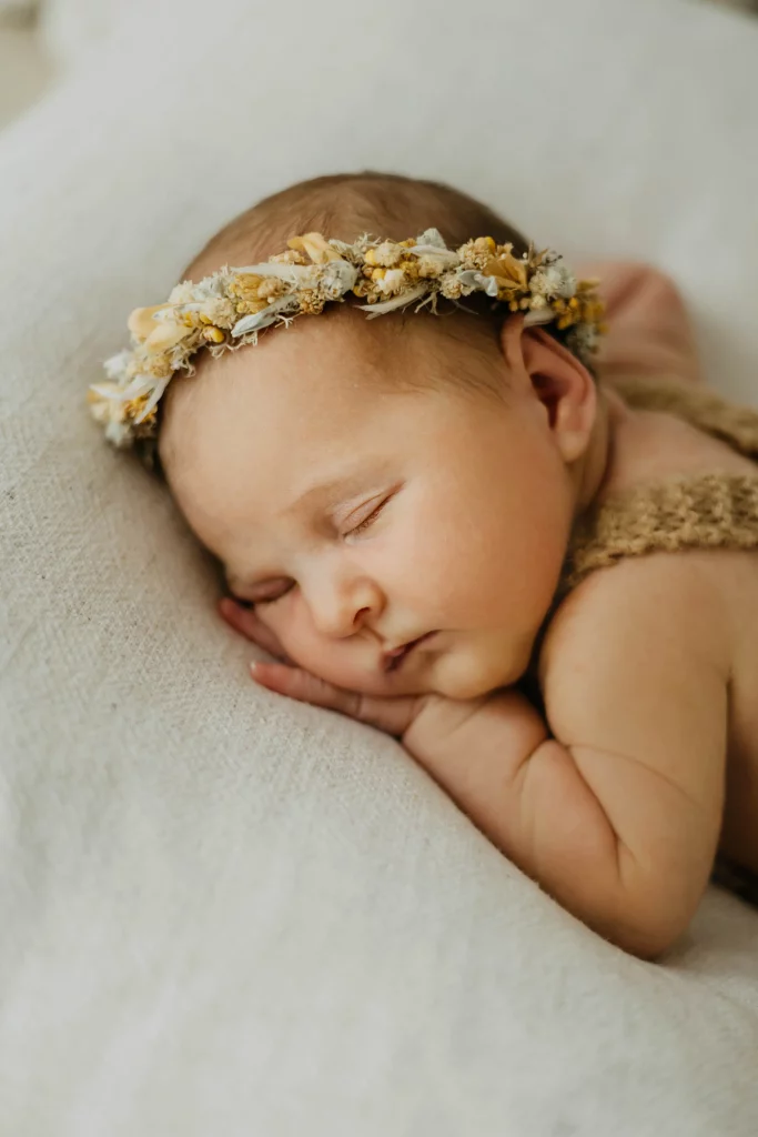 Neugeborenes schläft mit Blumenkranz und Hand unter dem Gesicht fotografiert von Familienfotografin Katja Stumbeck