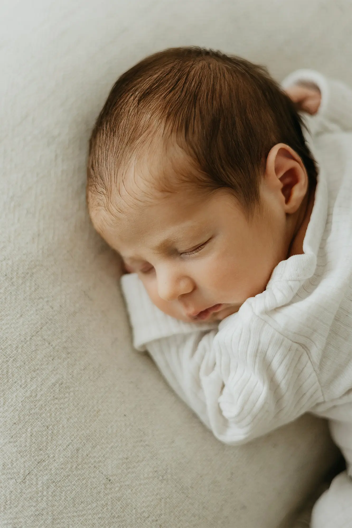 Ein neugeborenes Baby im Bayerischen Wald hat seinen Kopf auf seine Arme gelegt und schläft friedlich auf einem beigefarbenen Kissen